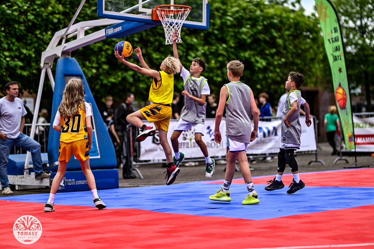 kinderen spelen buiten basketbal op een rood-blauw veld.