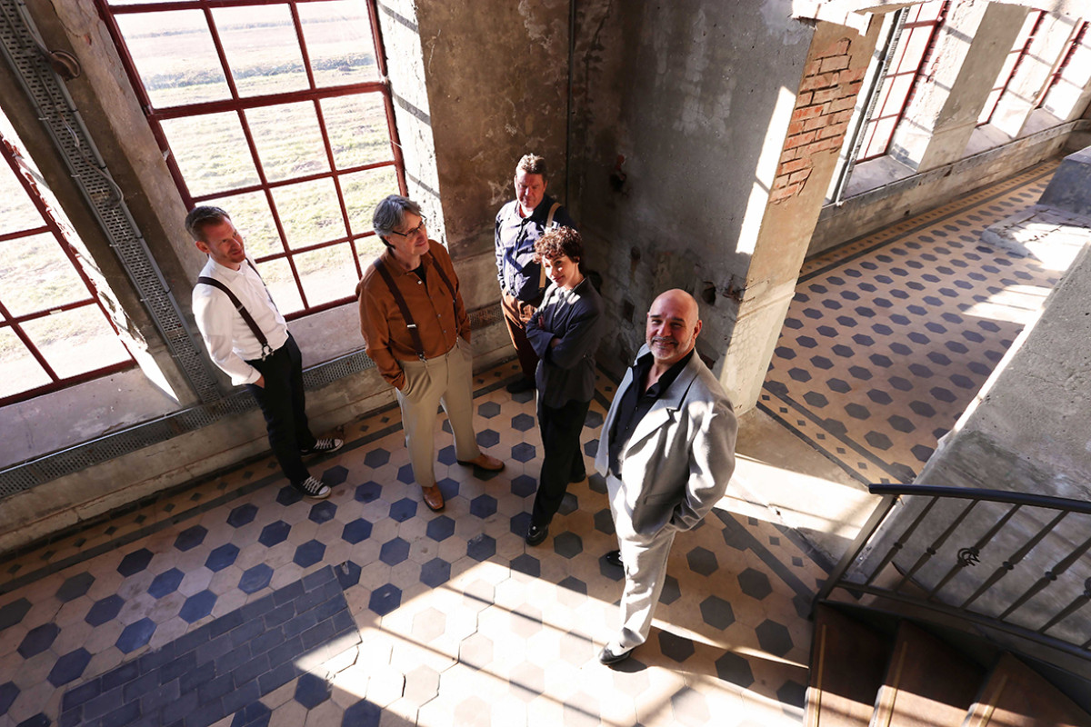 4 mannen staan in een oud gebouw en kijken naar boven waar de camera is.