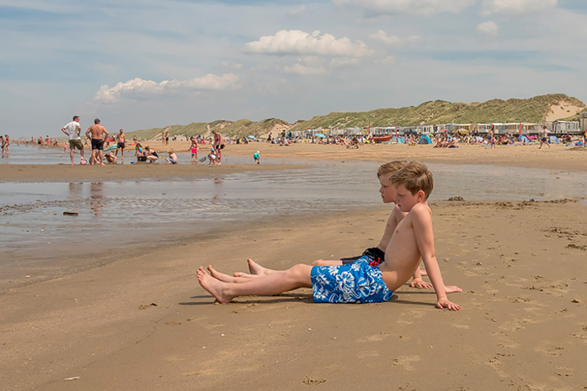 Twee jongetjes zitten op een zonnige dag in de branding op het strand van Heemskerk.