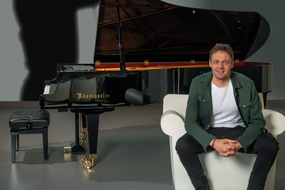 Man zit op een witte stoel, erachter een piano