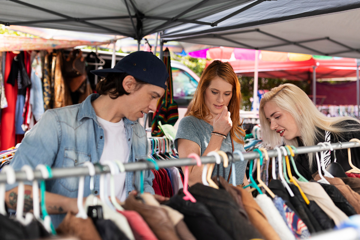 3 mensen bekijken kleding in een marktkraam
