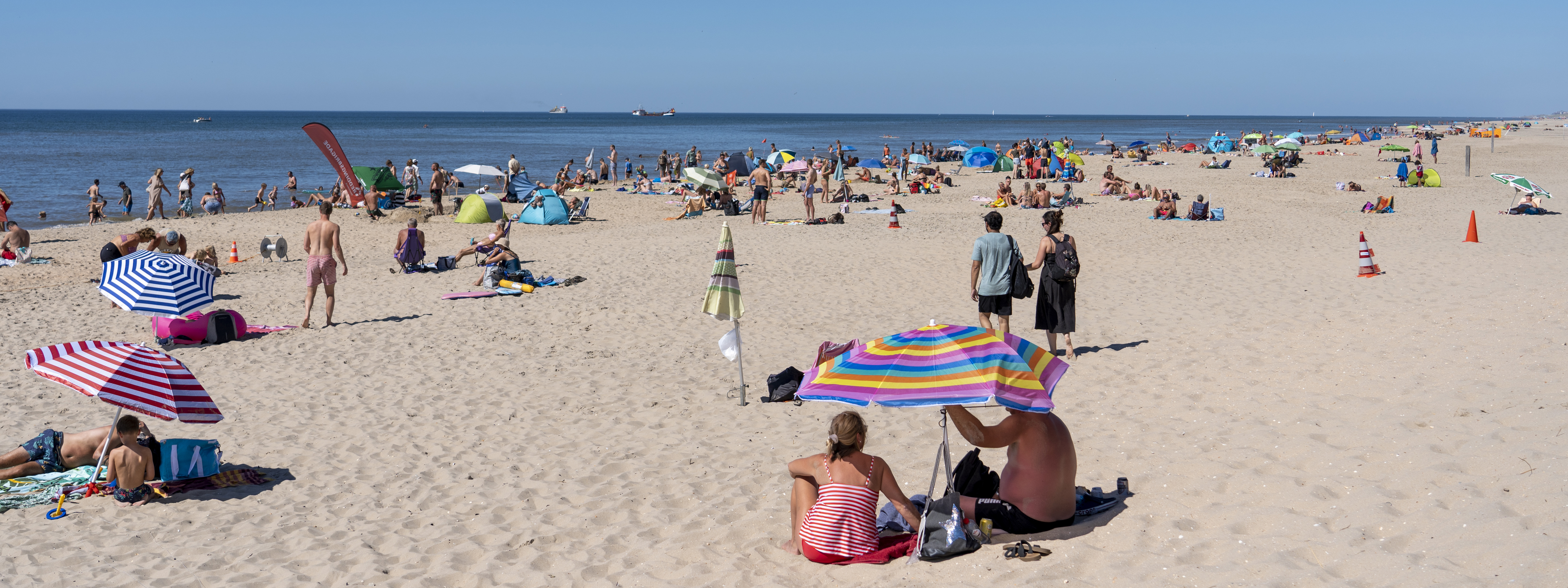 Mensen in zomerkleding onder een parasol op het zandstrand.