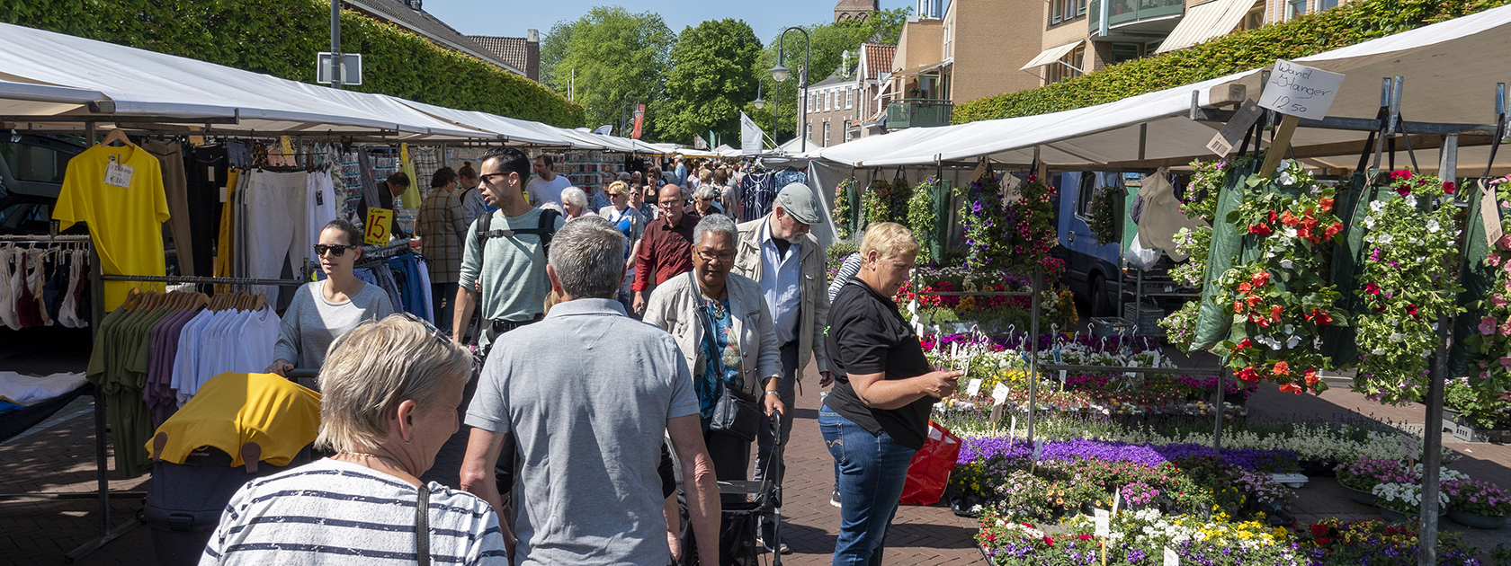 Mensen winkelen op de vrijdagmarkt met bloemen en kleding.