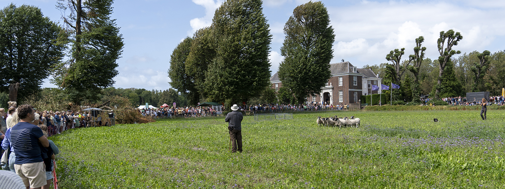 Grasveld voor Chateau Marquette waar een kring mensen omheen staat. In het midden staat een schapenherder met een paar schapen.