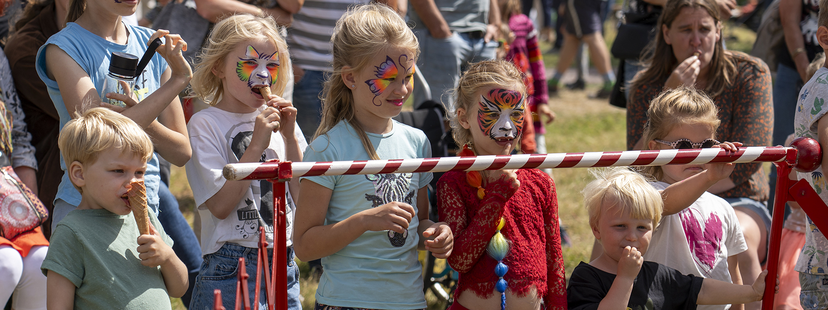 Kinderen met geschminkte gezichten en een rood-wit gestreefde omheining. Vrolijke kleuren en speelse sfeer.